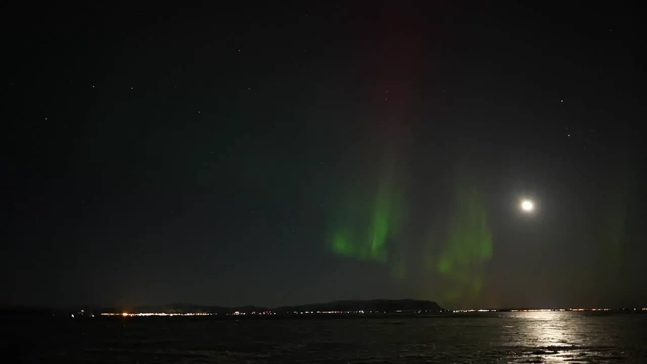 Panning shot showing flickering red and green northern lights over iced lake on Iceland