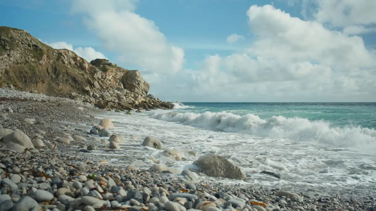 4K Cinematic landscape shot of waves hitting a rocky beach on a sunny day at Church Ope on the island of Portland in Dorset England