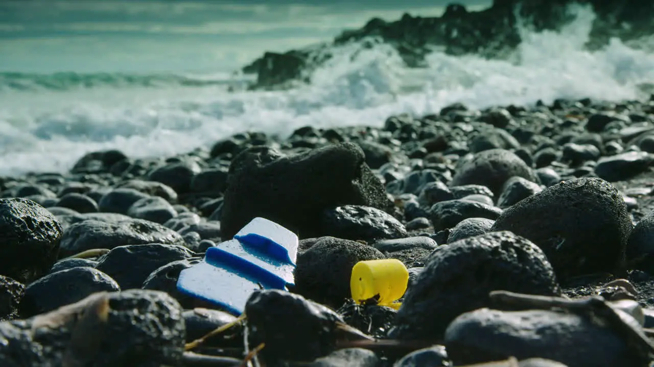 Stunning low level shot of a wave washing over plastic rubbish on a pebbly beach