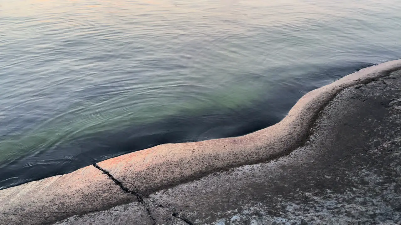 Small waves hitting rock shore during sunset creating peaceful atmosphere