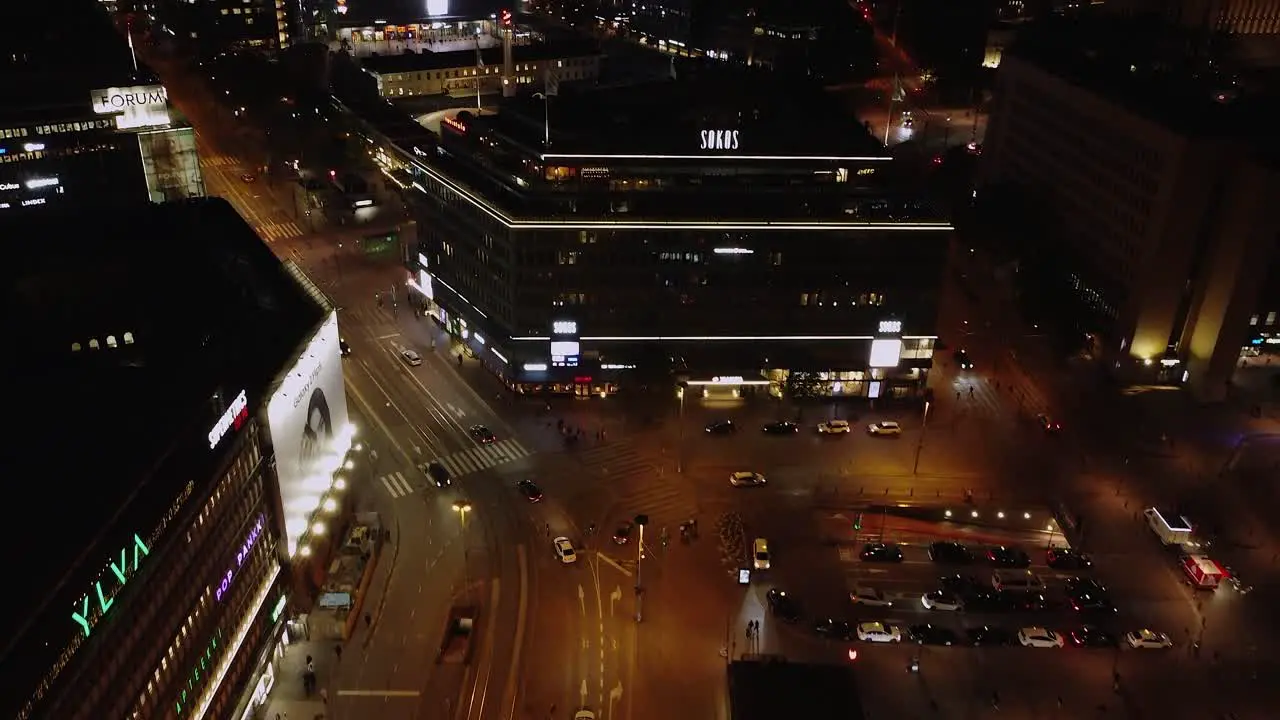 Night aerial tilts up from dynamic shopping plaza in downtown Helsinki