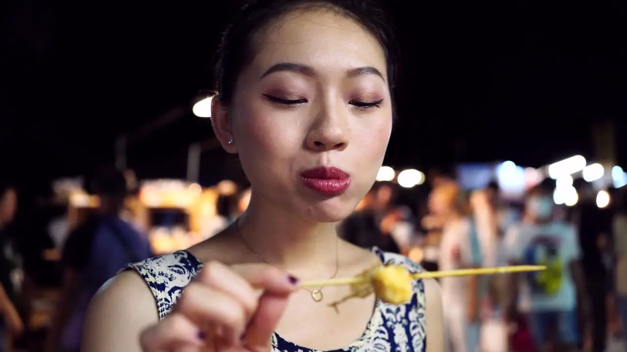 Asian woman eating fried quail eggs in night market