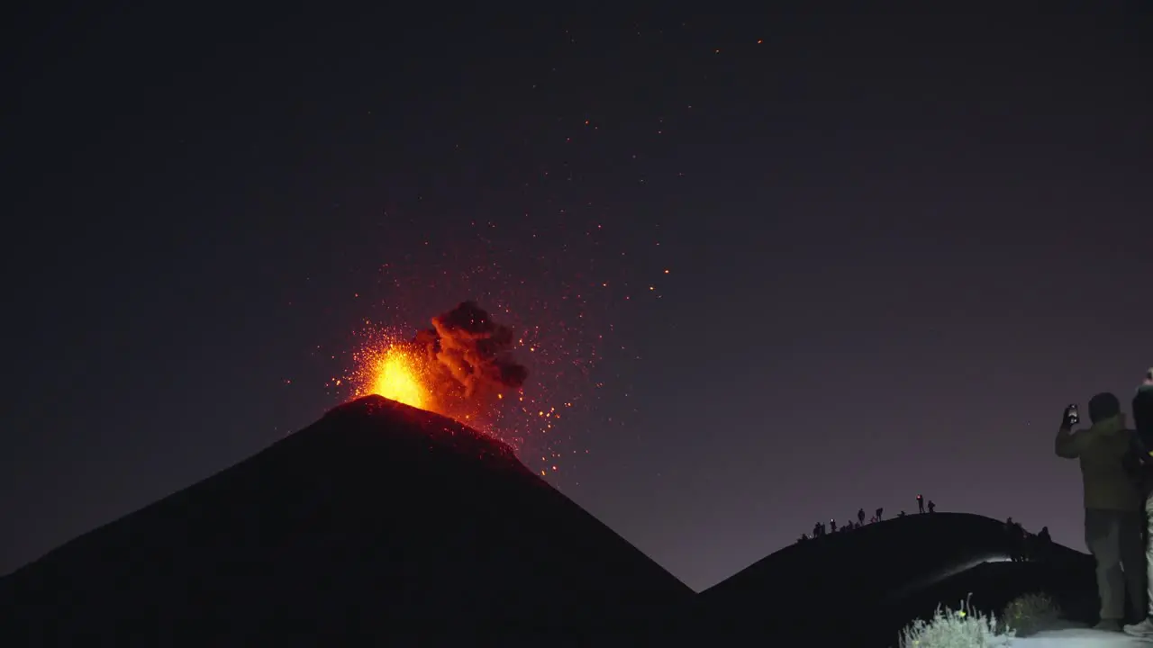 Massive Fuego volcano eruption at night with onlookers capturing explosive glowing lava and ash spectacle