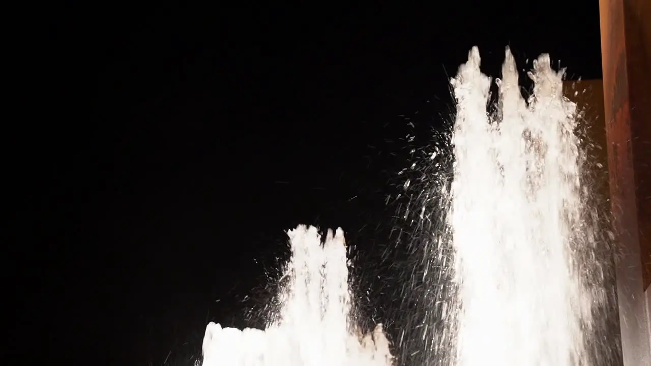 Low angle shot of white splashing water streams of fountain against black night sky with crescent half moon