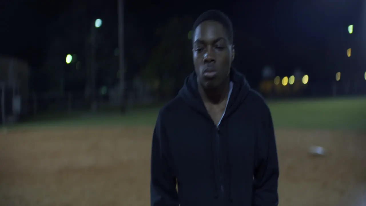 African American Teen Walks on Baseball Field at Night Front Medium