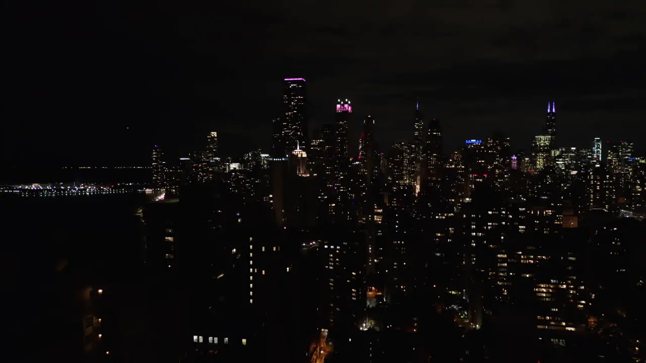 Aerial drone backward moving shot along the multiple high-rise buildings in congested downtown area of Chicago USA at night time