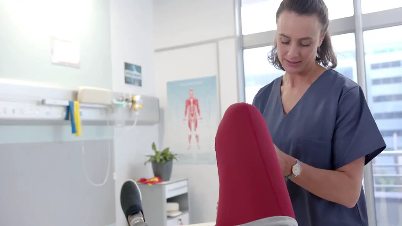 Caucasian female physiotherapist stretching leg of female patient at rehab center