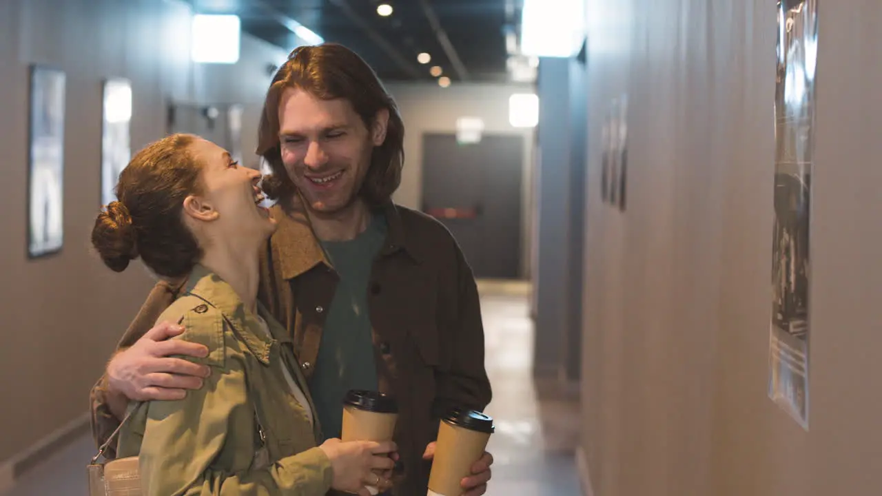 Pareja Feliz Con Una Bebida Para Llevar Hablando Juntos Mientras Miran Un Cartel De Pared En El Cine 2