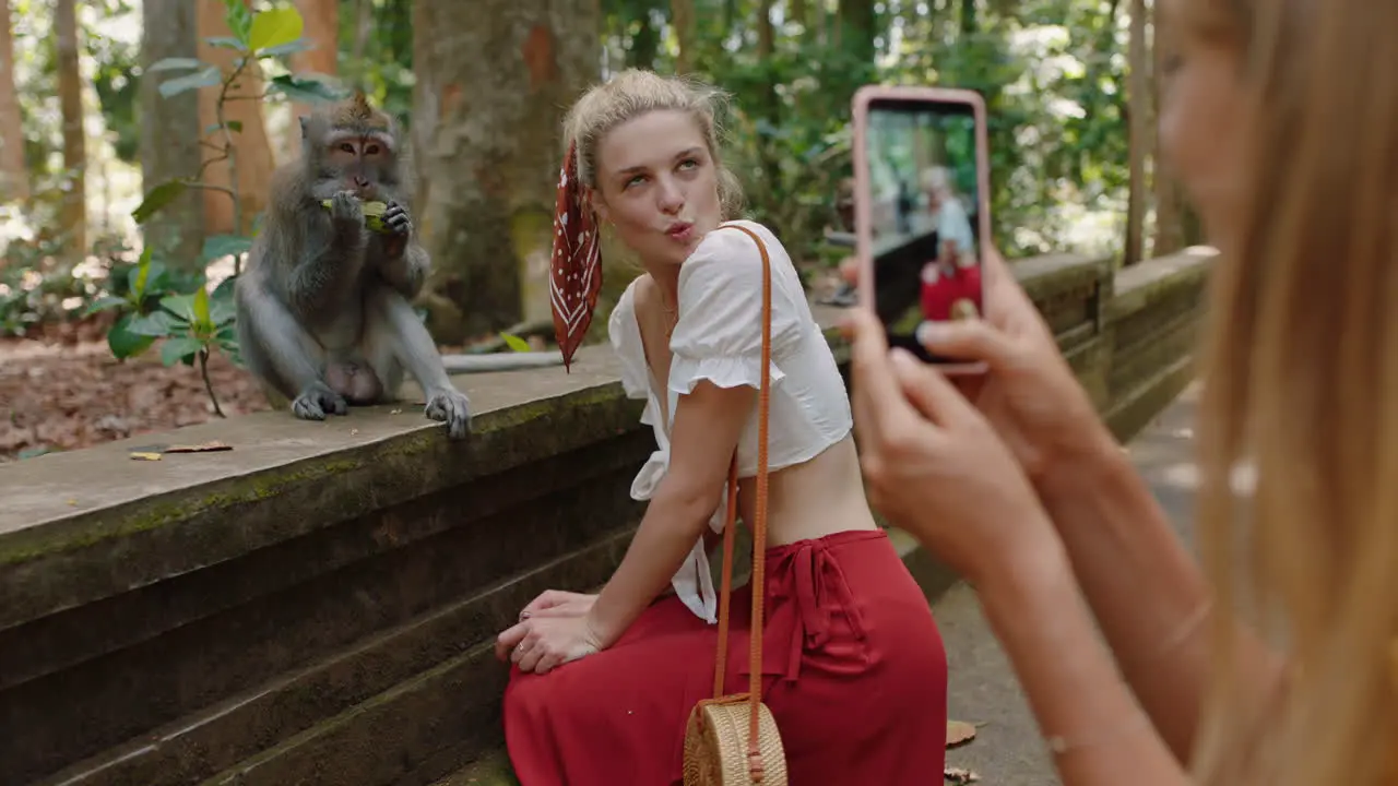 tourist woman using smartphone taking photo of friend posing with monkey in wildlife zoo having fun sharing travel adventure