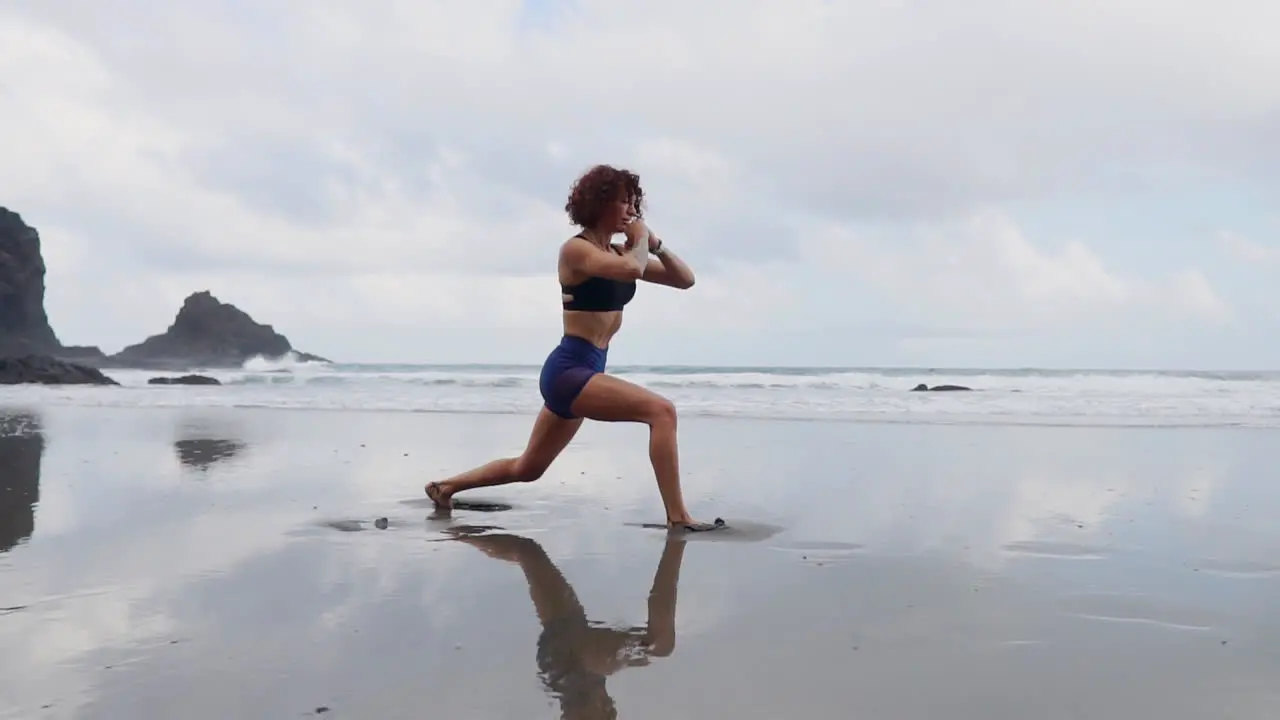 A young slender woman engages in stretching and yoga by the ocean's edge her gaze set on the horizon all captured in slow motion