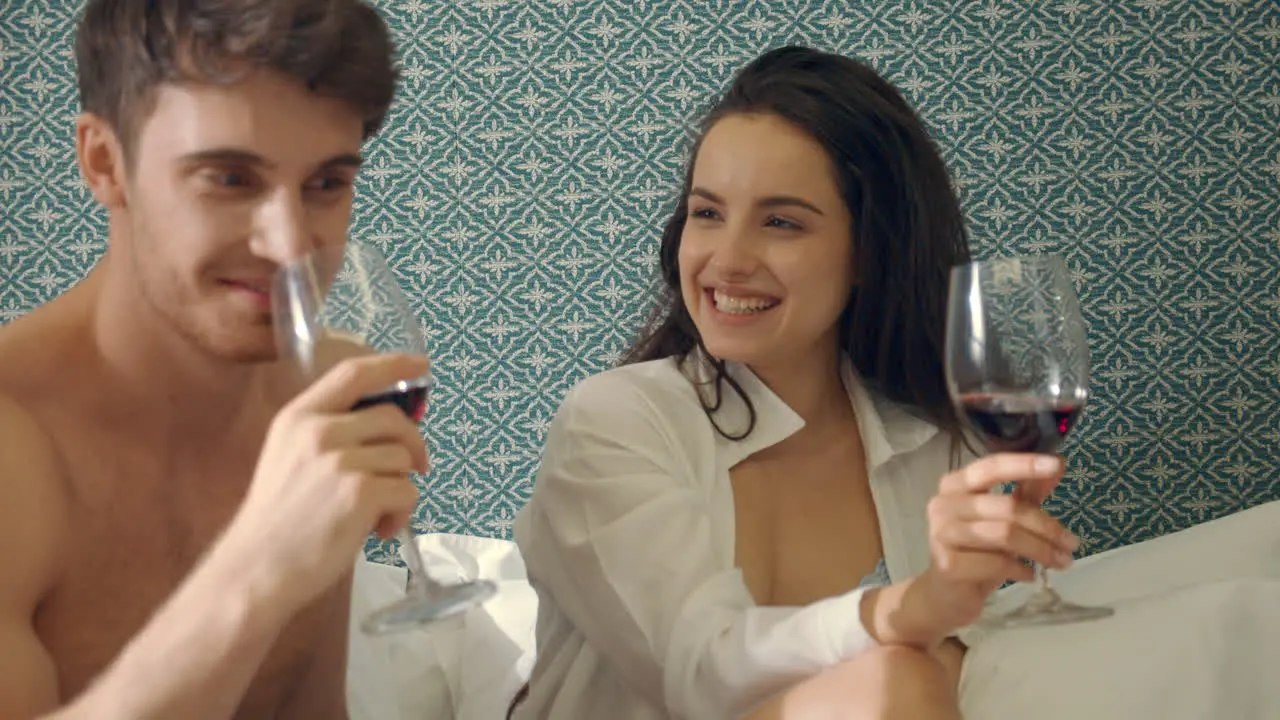 Cheerful couple raising toast glasses wine in bed Charming lovers having fun