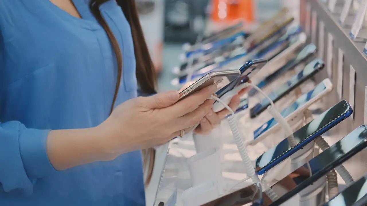 Closeup of woman's hand choosing for buying a new smart phone near a shop window in an electronics store