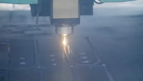 Close up of laser cutting of metal sheet with bright sparkles at factory