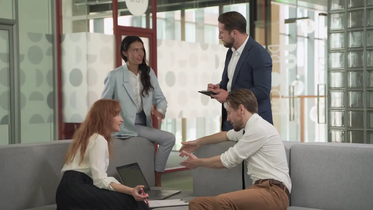 A Business Working Group Consisting Of Two Women And Two Men Have A Relaxed Meeting In The Armchairs In The Common Area Of The Offices 3