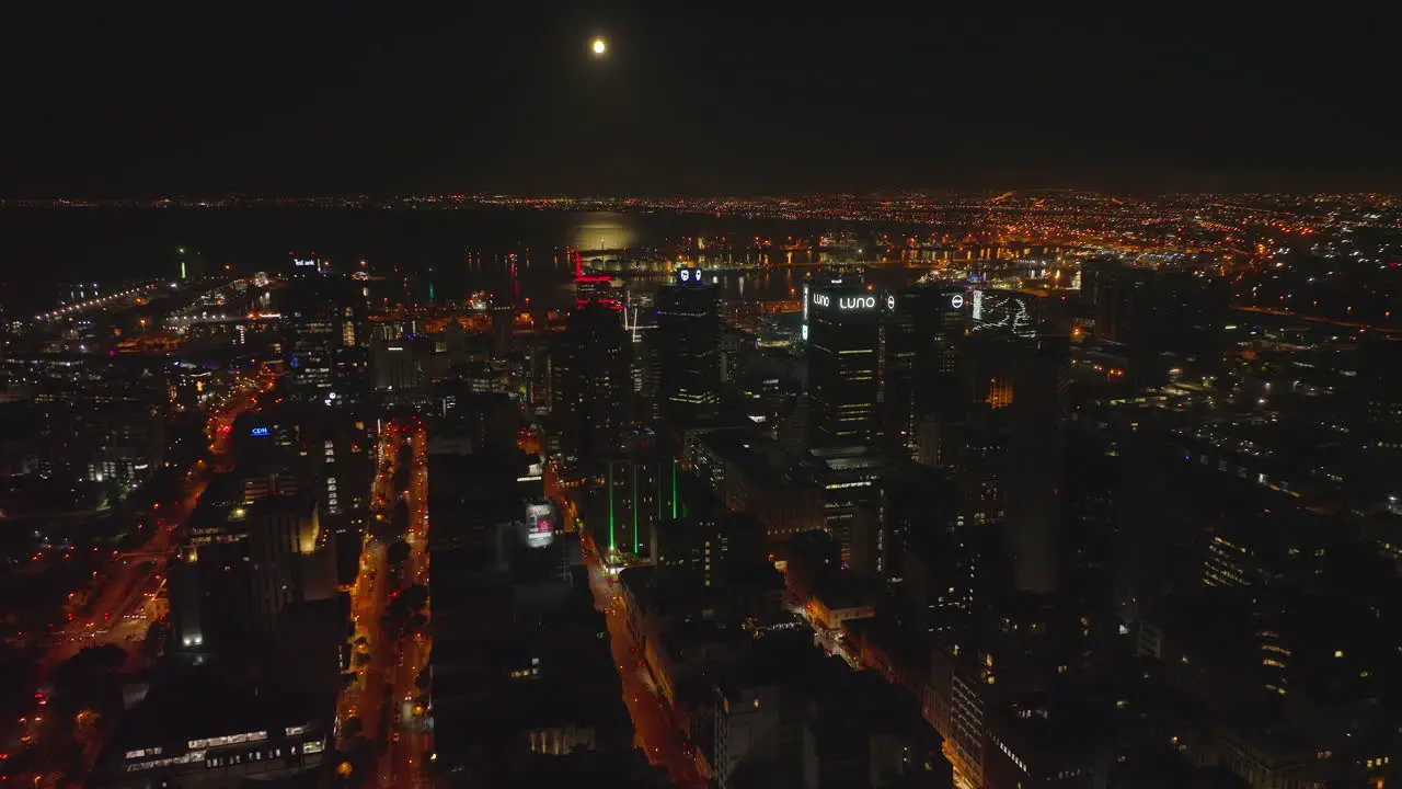 Fly above city at night Colour illuminated streets and tall office buildings in city centre Seaport in Table bay in background Cape Town South Africa