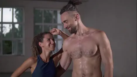 Happy couple with dreadlocks after successful training in sports club together Sport woman looking on her shirtless handsome partner or trainer smiling to each other embracing