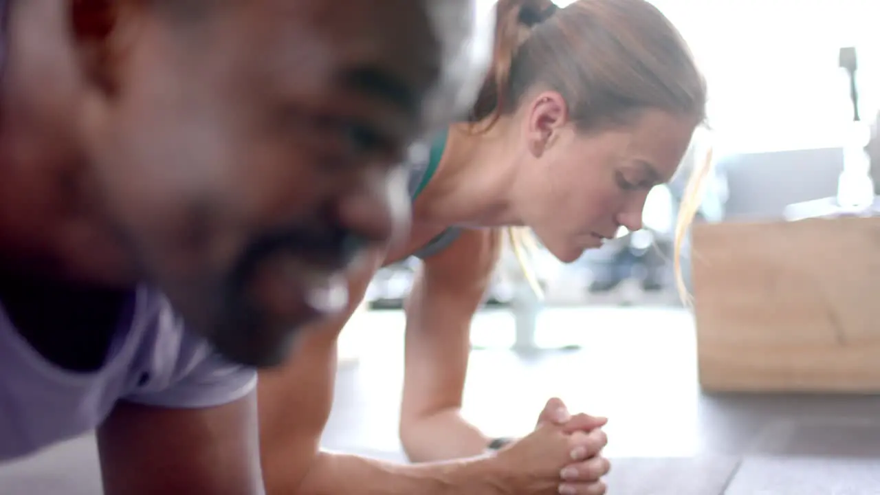 Fit African American man and young Caucasian woman exercising together at home