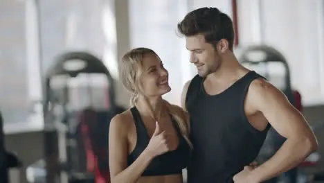 Happy couple showing thumbs up gesture after successful training in fitness club