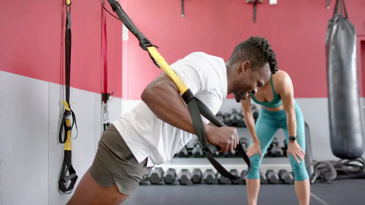 Fit African American man coaches a young Caucasian woman at the gym