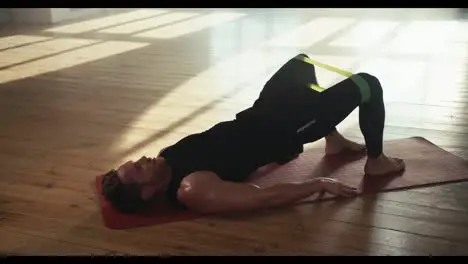 A man in a black sports summer uniform is doing exercises to strengthen the muscles of the pelvis and budur with the help of a