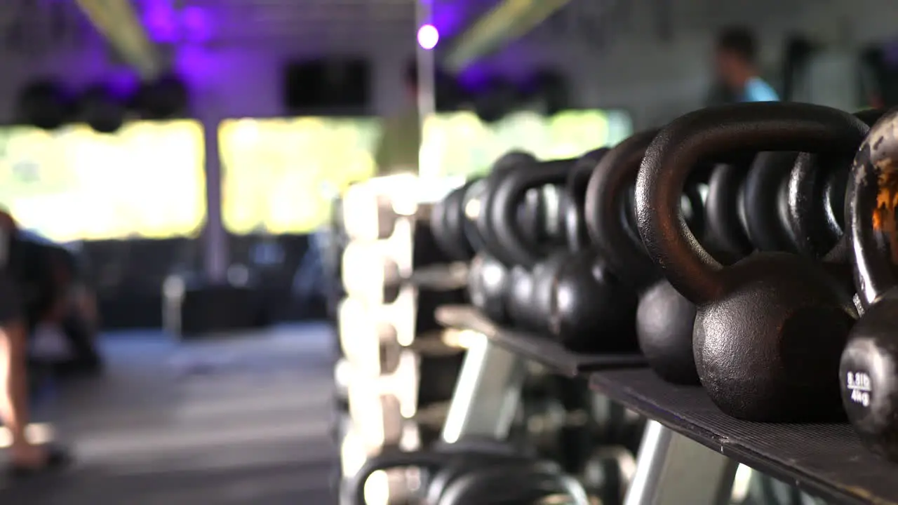 A rack of weights and kettlebells in a gym with people defocused working out and training in the background