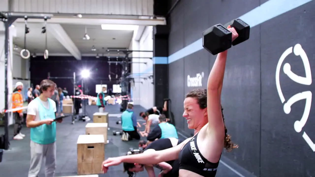 Grit and Strength Brunette Girl with Pigtails Pushing Through Snatches in CrossFit Competition Background Features Other Competitors