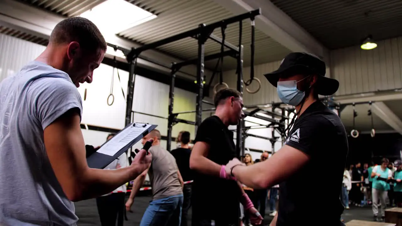 three muscular young Caucasian men slap fists to greet each other during a crossfit competition in a gym with other people behind them and weight equipment