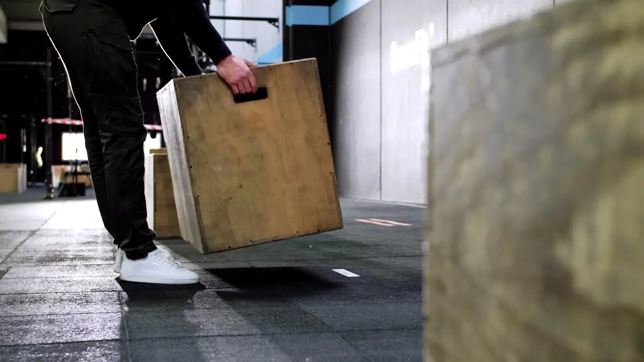 Man Placing Jump Box for CrossFit Competition in the Center of Rubber-Floor Gym Illuminated by Background Lighting