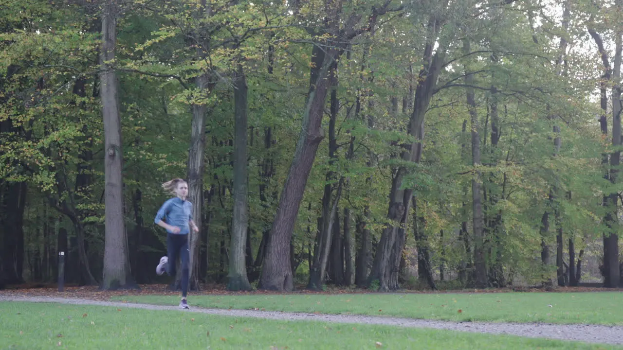 Dynamic shot of a woman running towards the camera in a grassy field at the park