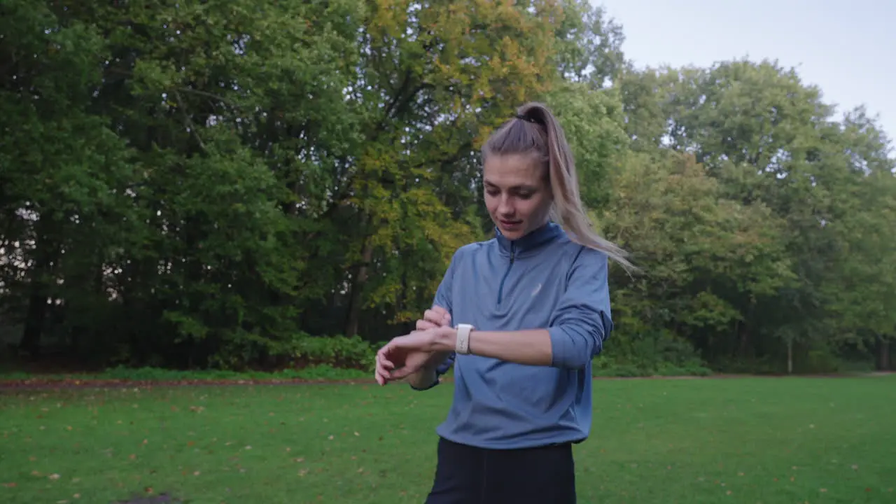 Captivating shot of a woman stopping mid-run in a grassy field at the park to check her digital sports watch