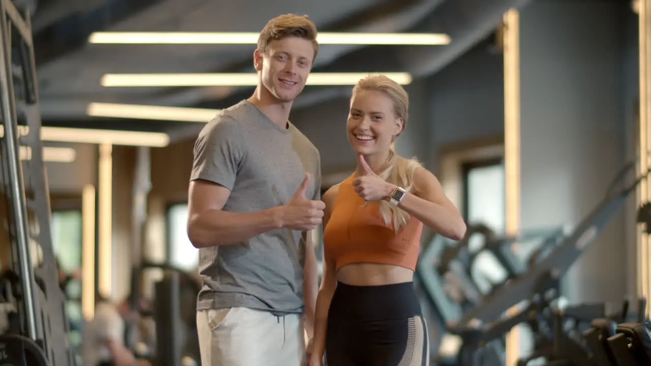 Winners couple showing like signs in sport club Couple enjoying results at gym