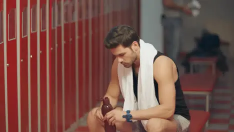 Tired sportsman drinking water in dressing room