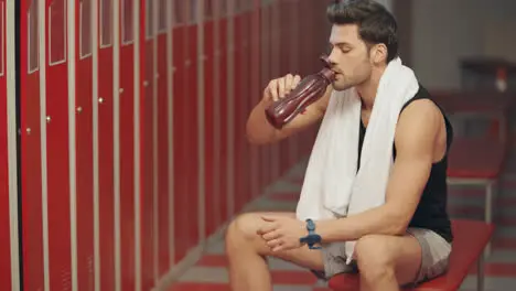 Closeup exhausted man sitting in dressing room with sport bottle