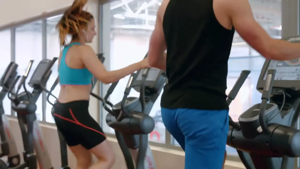 Fit couple using cross trainer in gym