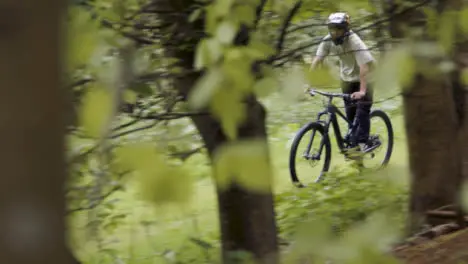 View Through Trees Of Man On Mountain Bike Cycling Along Trail Through Woodland 2