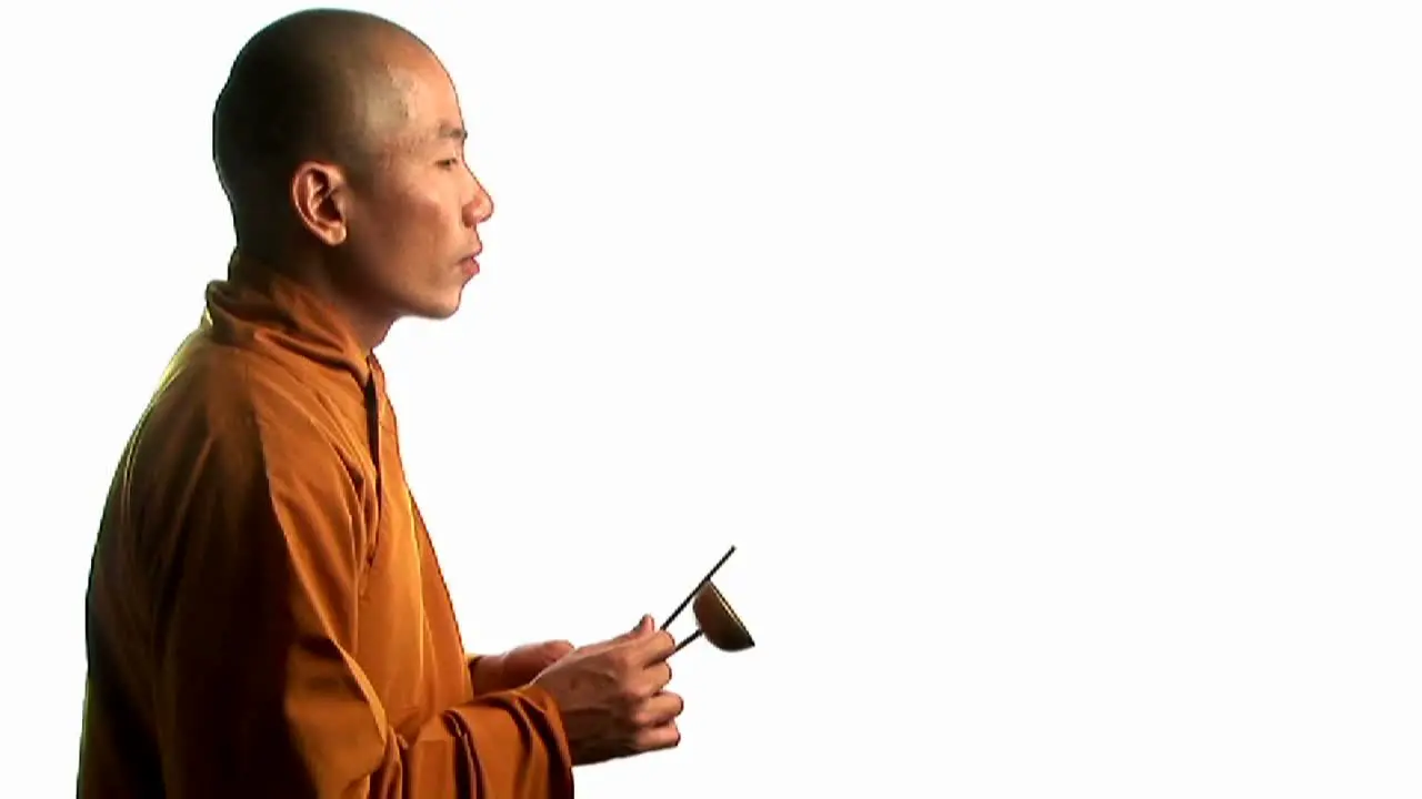 A Buddhist monk wearing an orange robe taps a bell with a small stick 2