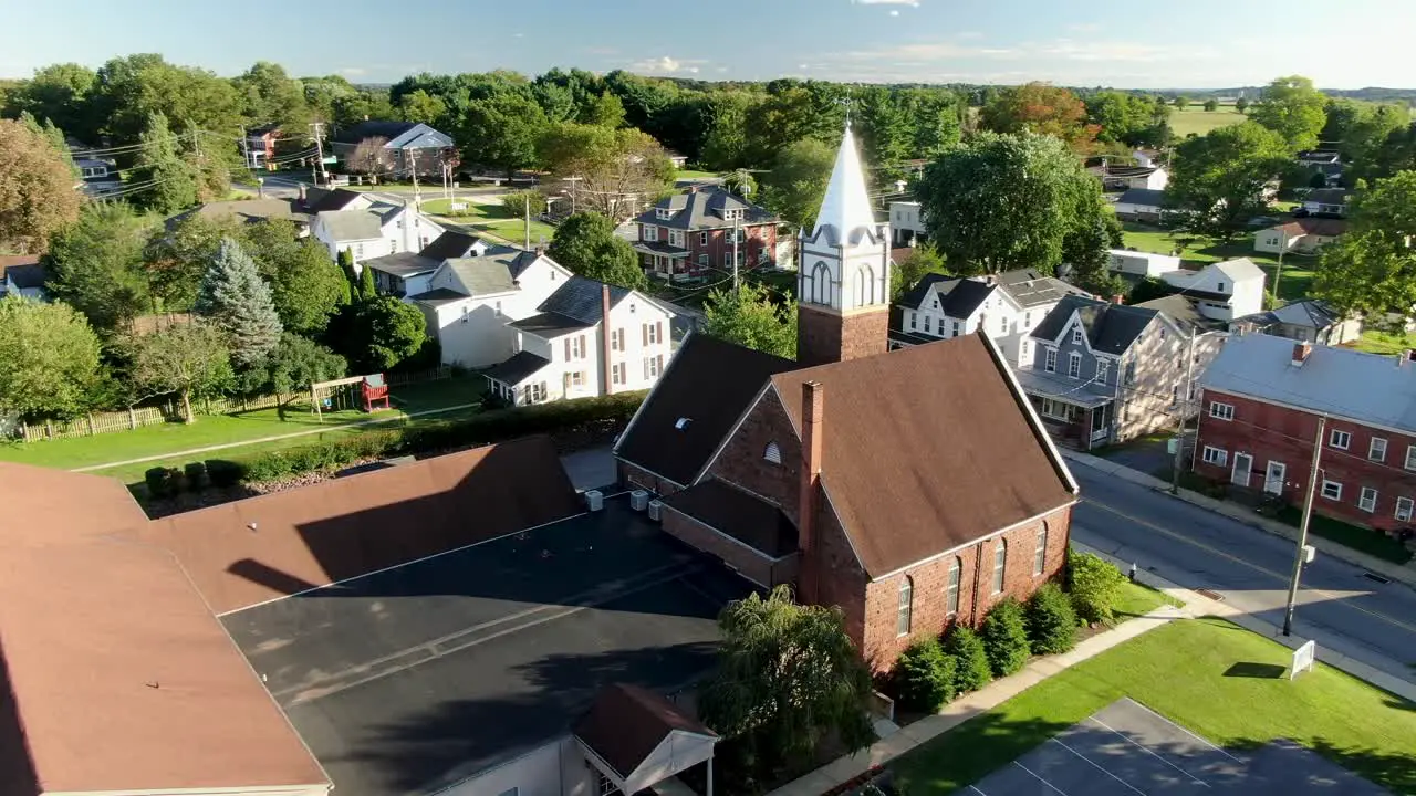 Christian religion in America United States small town with old brick church and steeple along street with neighborhood houses during summer aerial orbit shot