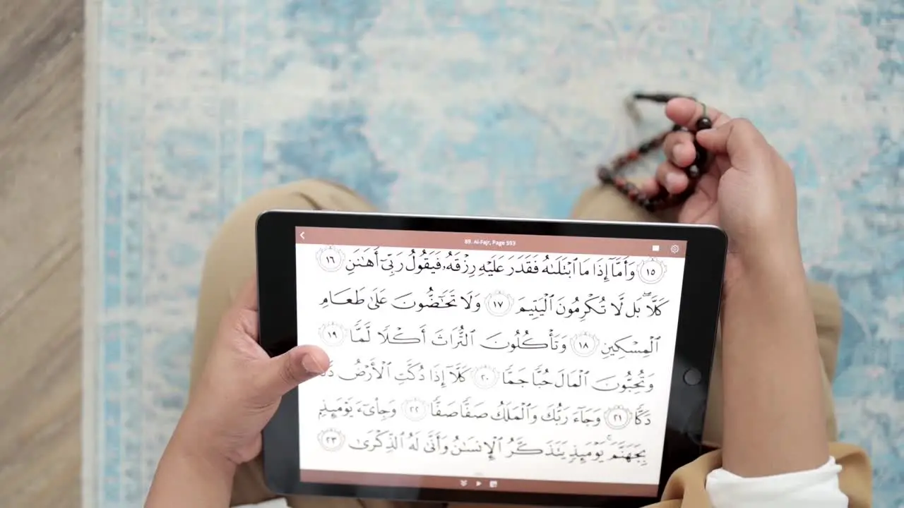 reading Quran scripture from iPad holding prayer beads Islamic Dhikr