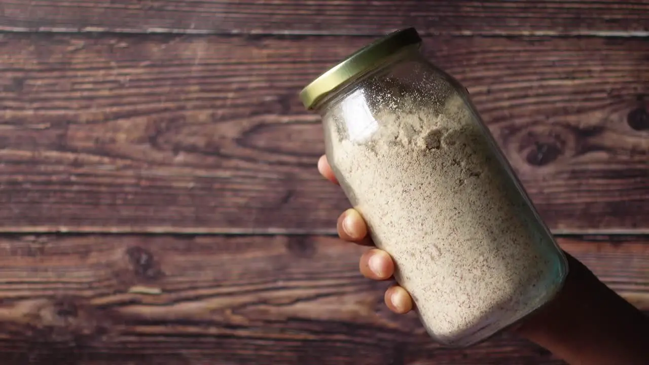 Hand hold a glass jar of a almond powder 