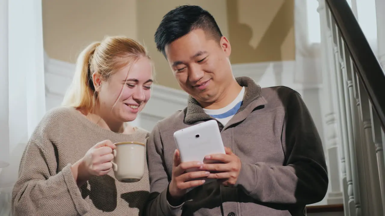 Young Couple Enjoys Tablet In House Sitting On Stairs