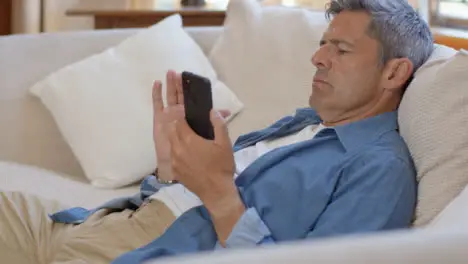 Medium Shot of Middle Aged Man Slouched On Sofa Using Smartphone 