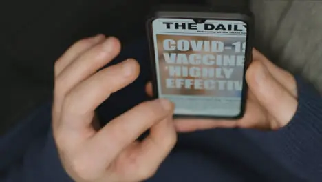 Close Up of Hands Scrolling COVID Vaccine News Article On Phone