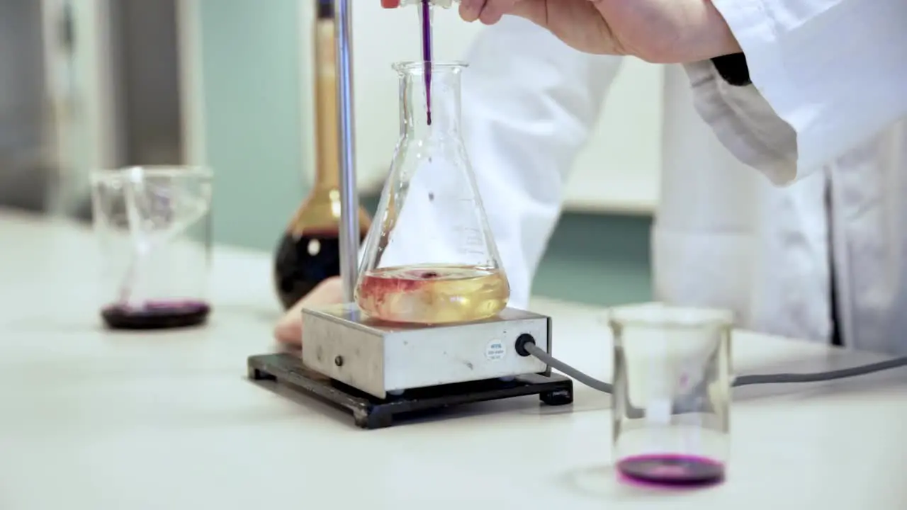 Slow motion shot of a scientist mixing different substances in a glass wearing a white jacket in a lab