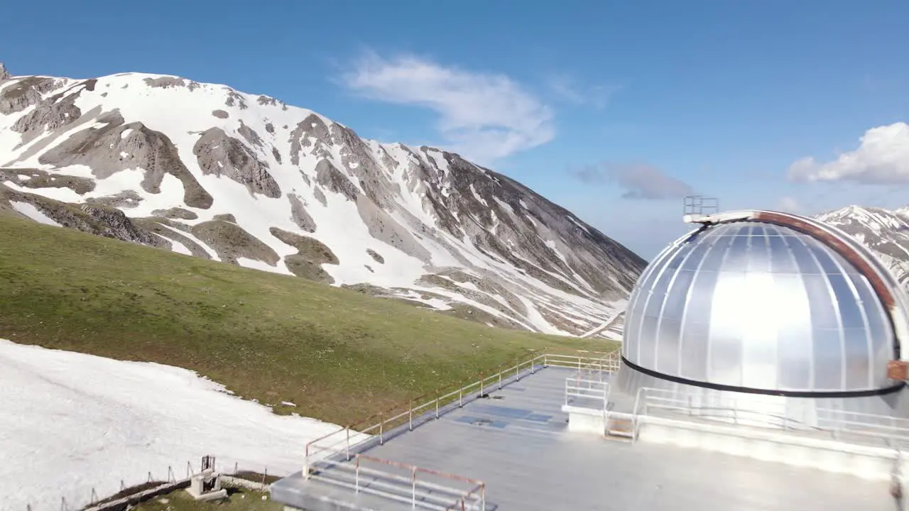 Wide angle drone shot flying towards an observatory located on top of a mountain with an incredible mountains landscape in the distance in the region of Abruzzo in Italy during the winter