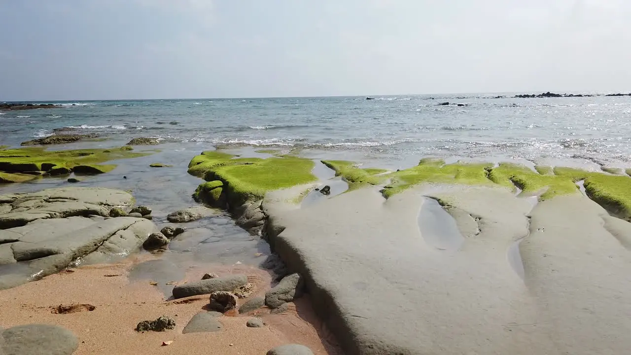 Side motion along the beach of a remote Andaman Island showing erosion of ancient volcanic rock at low tide with seaweed and reefs