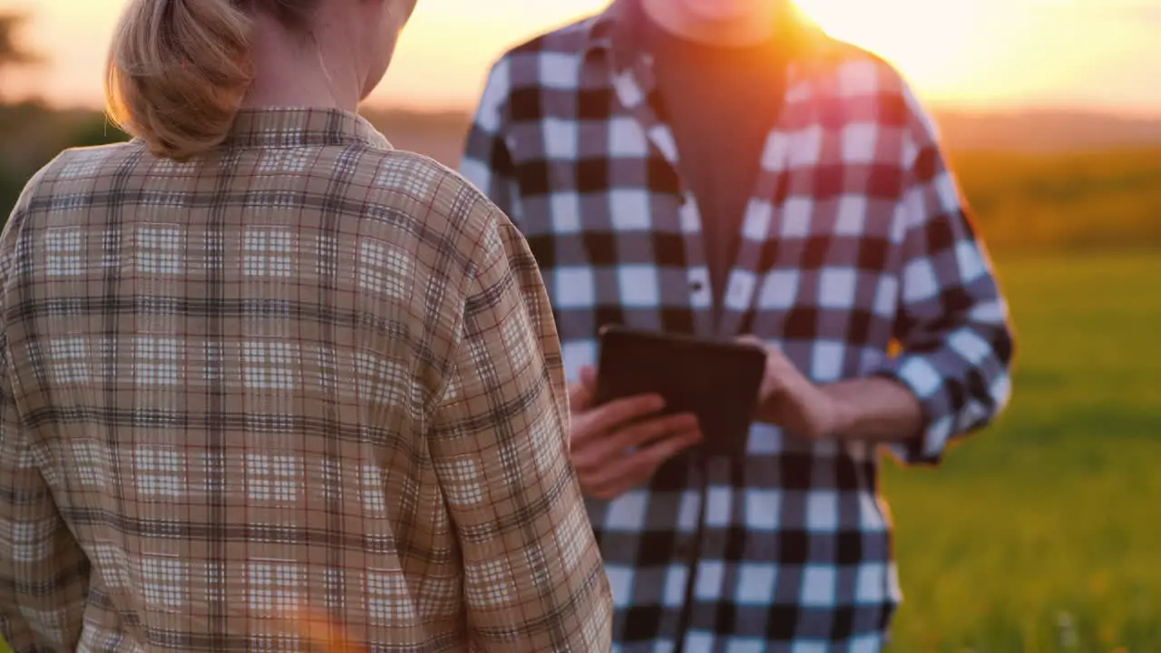 Man And Female Farmers Work In A Field At Sunset Use A Tablet