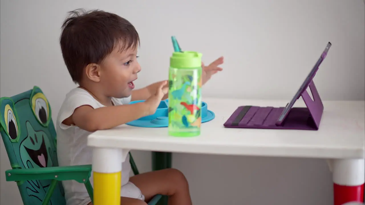 Cute latin Toddler watching a movie on a tablet while eating breakfast sitting on a baby table