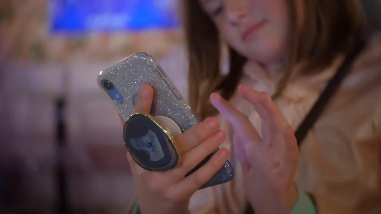 Girl using phone with bling phone and poppet at night in cafe