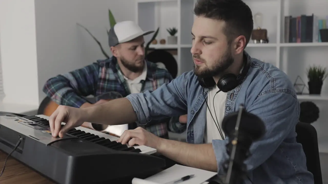 Young Male Musicians Creating Playing Guitar And Electric Keyboard At Home