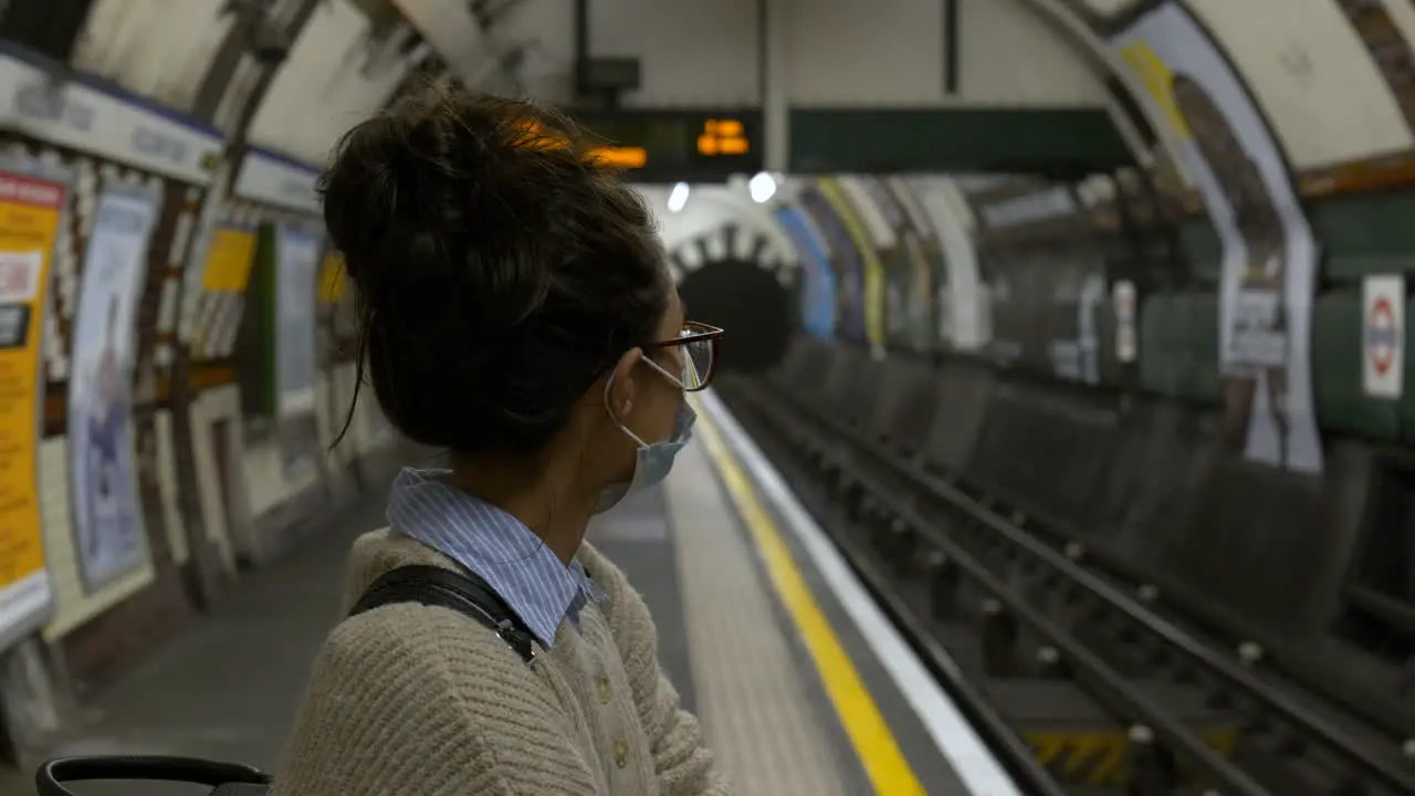 Woman wearing a face mask waits in an empty tube station London UK